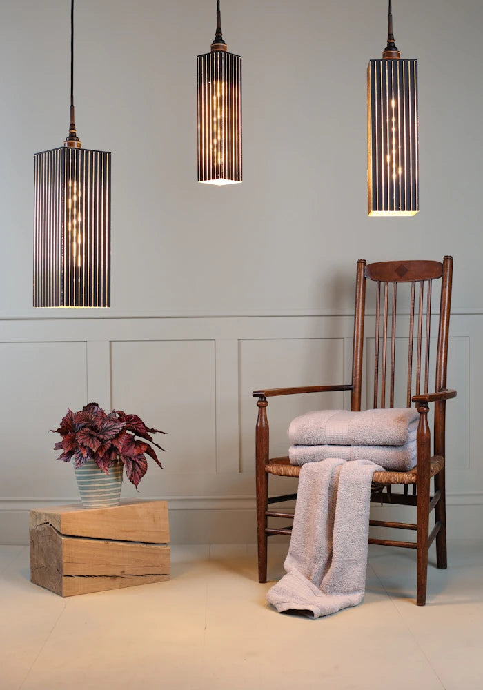 Triple black and gold bathroom pendant light cluster with plant, wooden chair and bath towels.