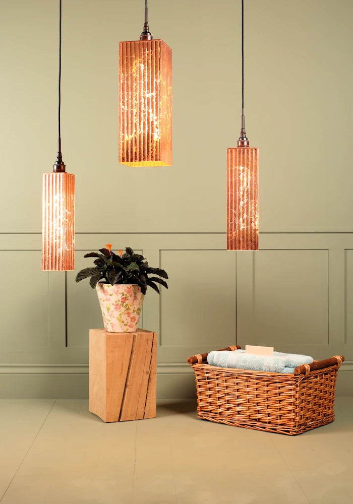 Large triple rectangular copper leaf cluster bathroom pendant light, plant and basket of bath towels.