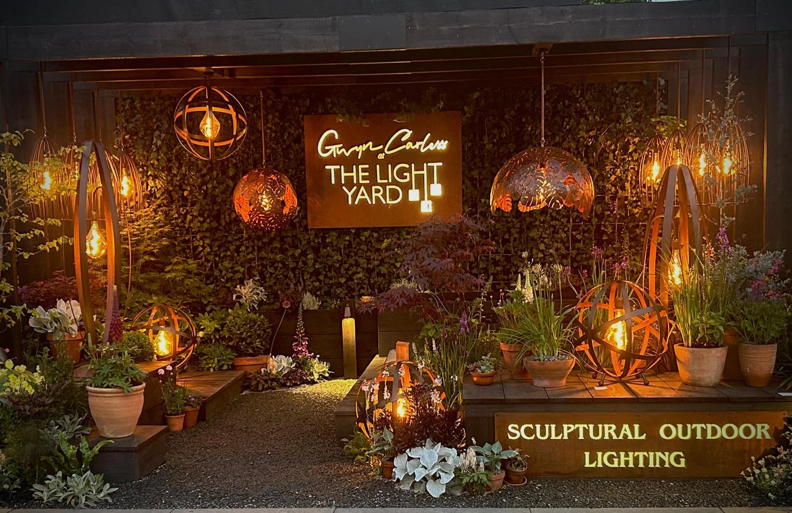 Outdoor lighting display with various lamps and plants, featuring 'The Light Yard' sign.