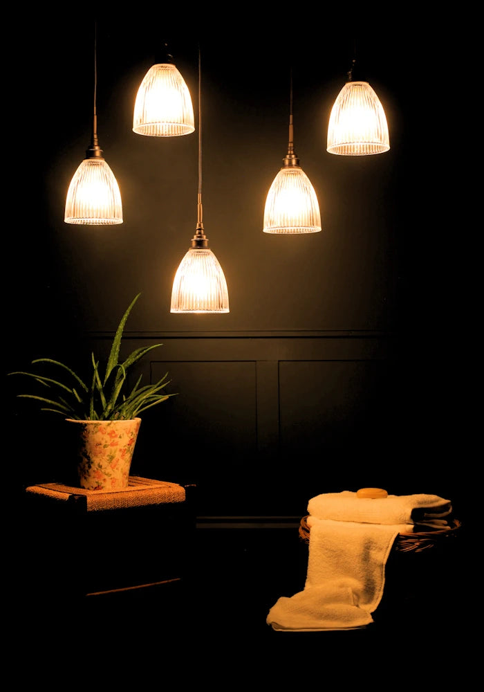 A cluster of five small bell prismatic glass bathroom pendant lights with green plant and towels in a basket.