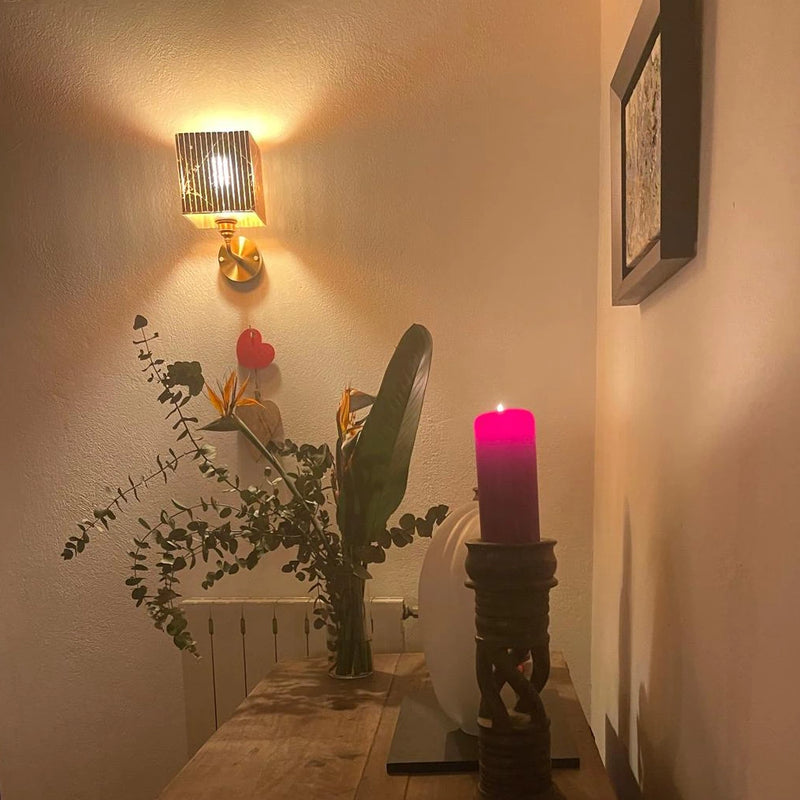 Decorative setup with a contemporary wall light, plants, and a candle on a wooden surface.