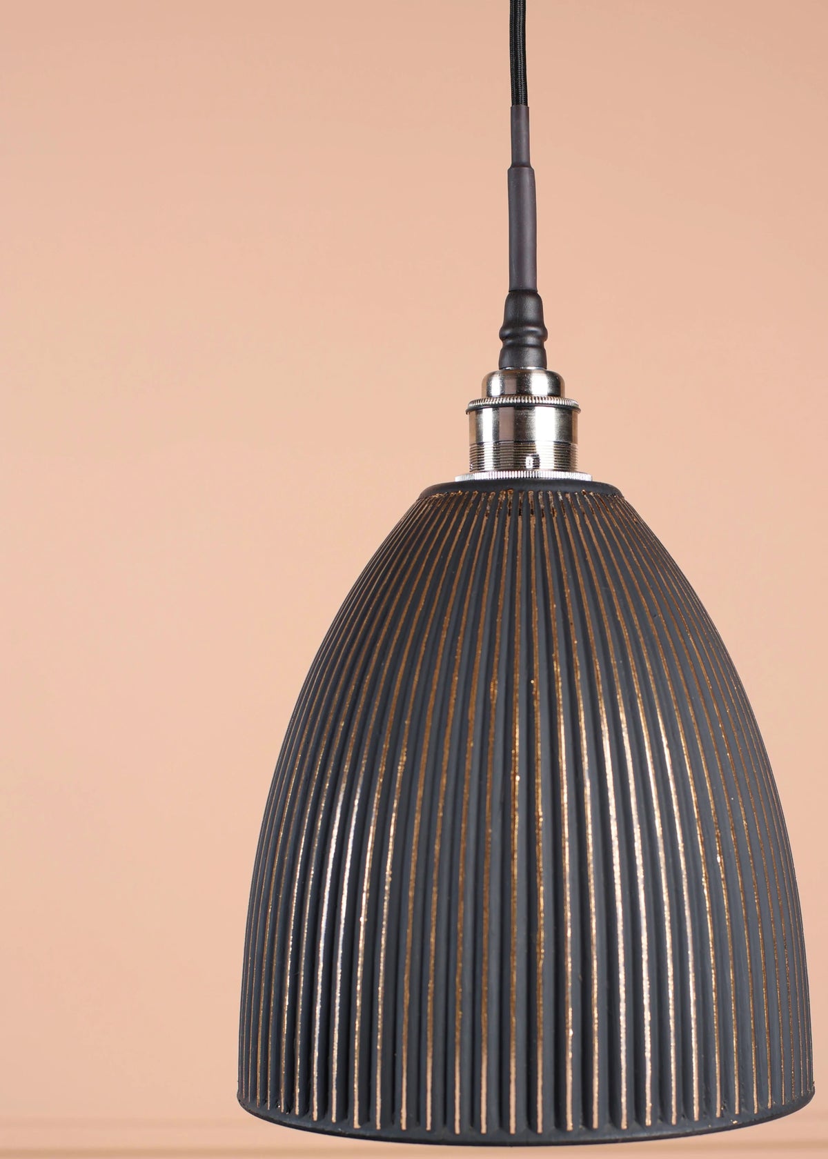 A dark gray ribbed dome pendant light hanging from a black cord against a warm beige wall with subtle molding details.