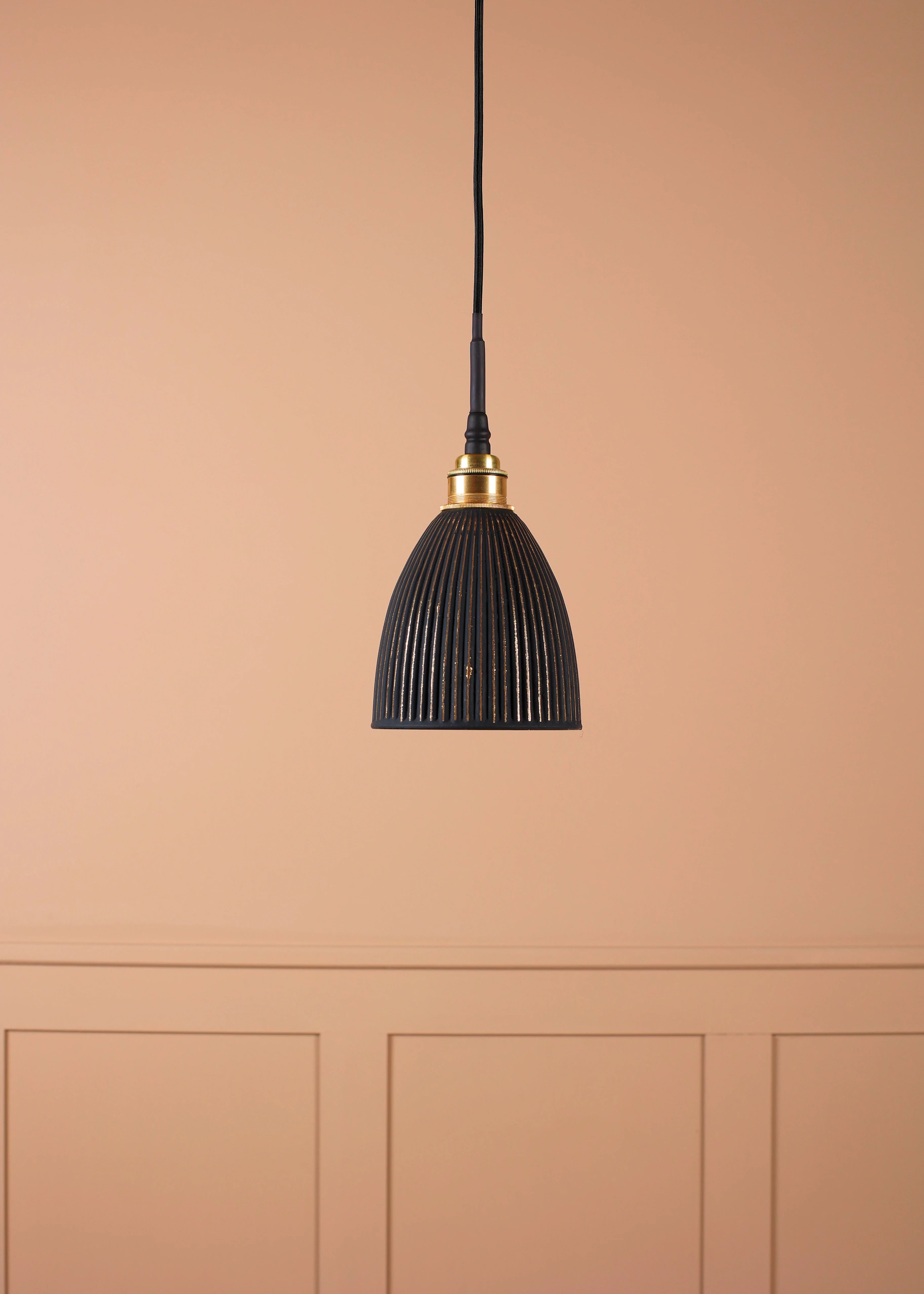 Black & gold bell shaped bathroom pendant light with brass lamp holder on tan coloured panelled background