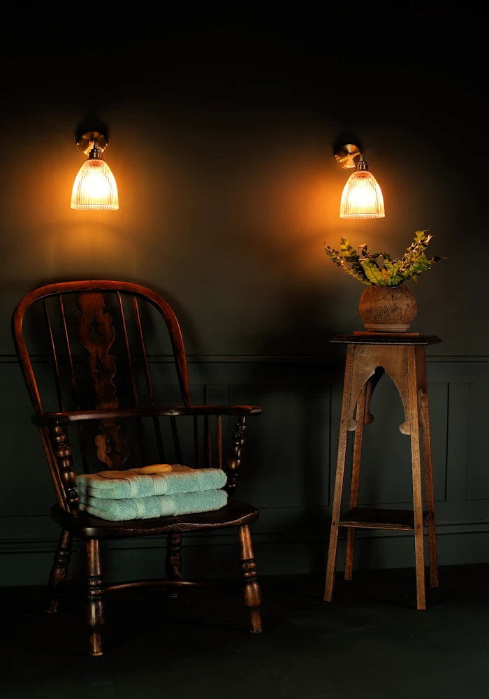 Elegant small bell glass IP44 bathroom wall lights, vintage wooden chair with bath towels, pot plant