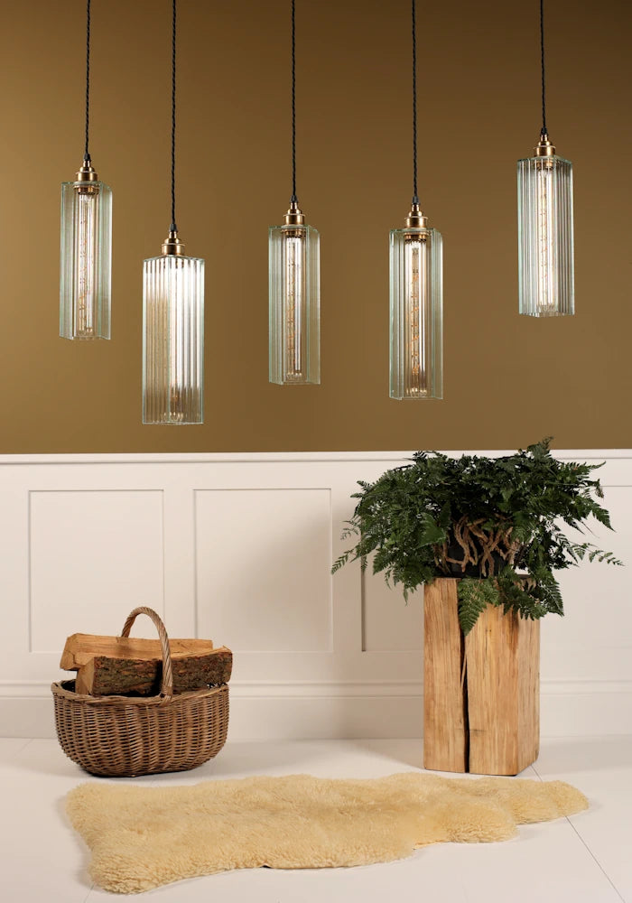 Modern pendant lights hanging above a room with a plant and basket on a wooden floor.