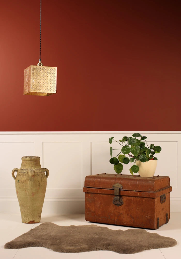 Cube gold leaf pendant light with Moroccan style pattern hanging over vase, vintage trunk, plant on red background