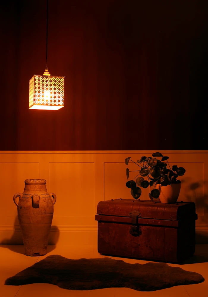 Cube gold leaf pendant light with Moroccan style pattern hanging over vase, vintage trunk in dimly lit room