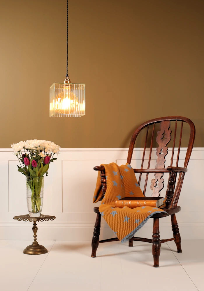 Wooden chair with an orange blanket, a small table with flowers, and a pendant light in a room.