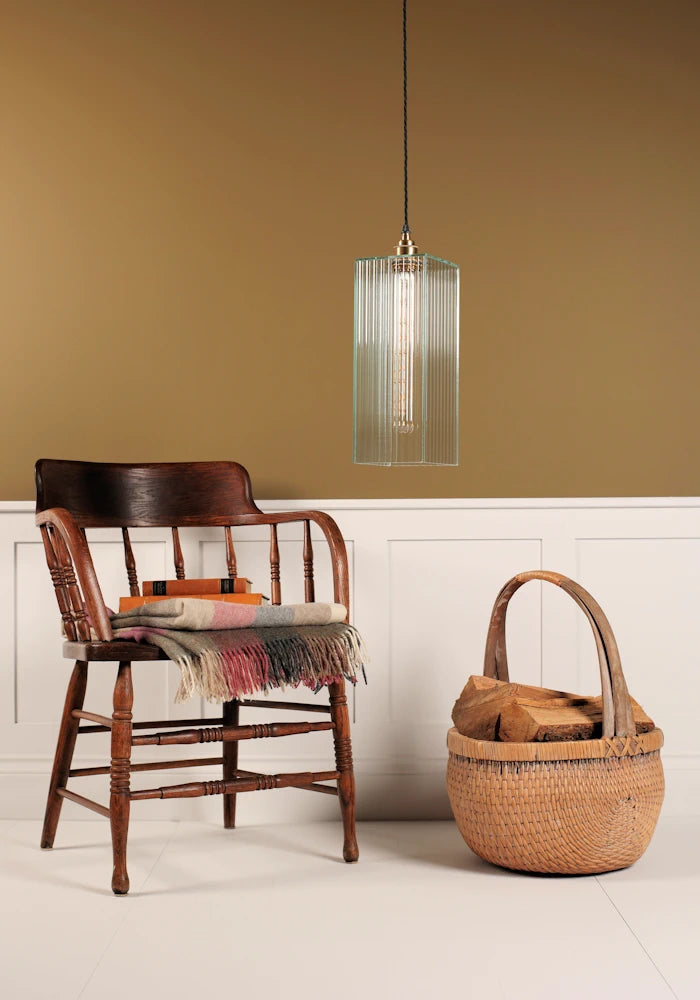 Statement ribbed glass pendant light hanging over chair with rug, basket of logs, on beige background