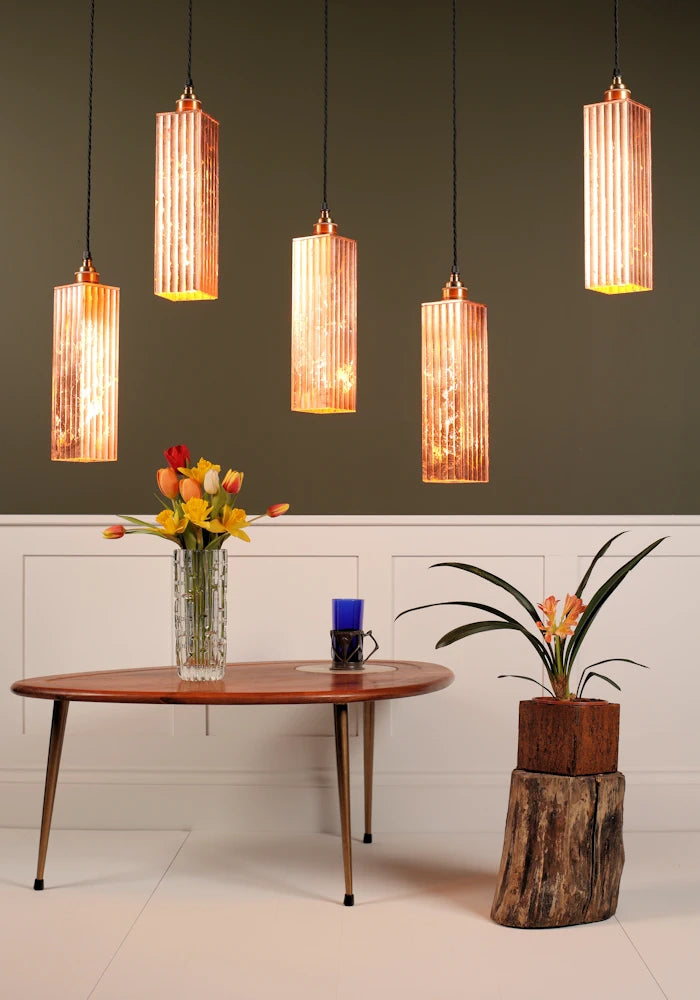 5 copper pendant light cluster hanging over coffee table with vase of tulips with green and white background.