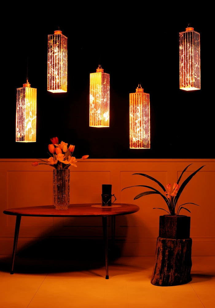 5 copper pendant light cluster hanging over coffee table with vase of tulips with dark background.