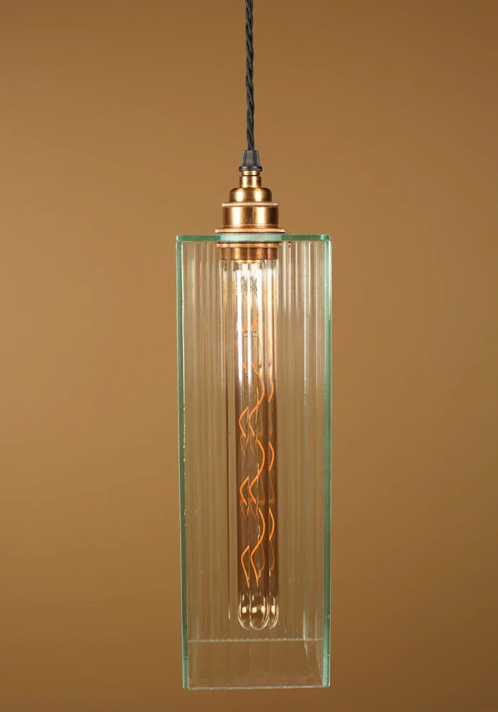 Glass pendant light with an exposed bulb, brass lamp holder against a brown background