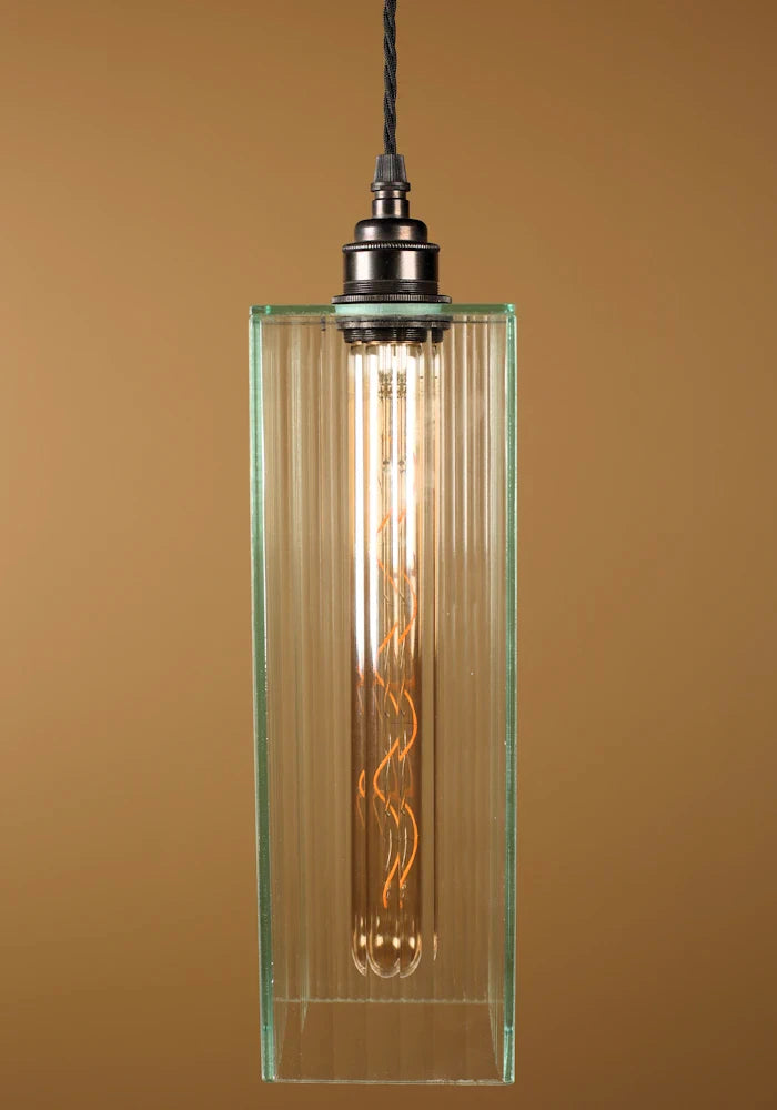 Glass pendant light with an exposed bulb, bronze lamp holder against a brown background