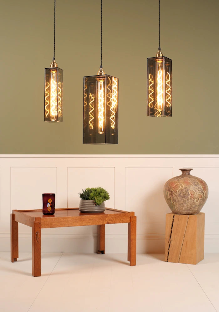 Three smoked glass pendant lights hanging above a wooden table with decorative items against a green wall.