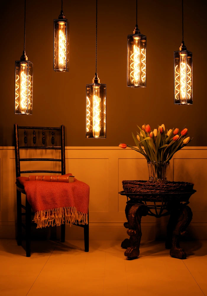 Vintage-style pendant lights hanging above a chair and table with flowers in a warm-lit room.