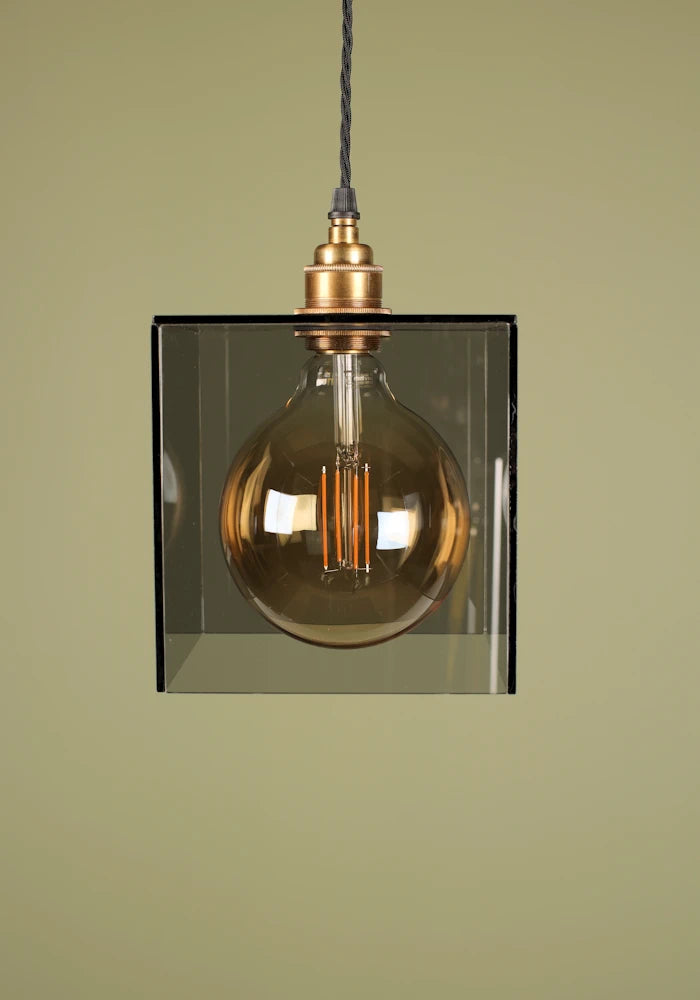 Vintage-style pendant light with a smoked glass shade, brass lamp holder and exposed bulb against a green background