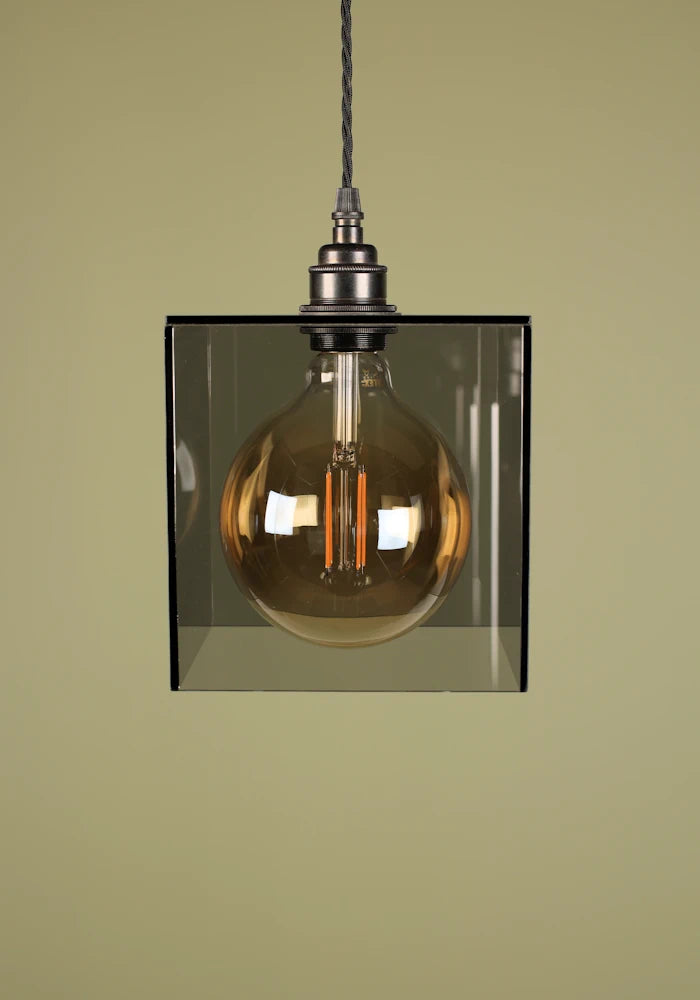 Vintage-style pendant light with a smoked glass shade, bronze lamp holder and exposed bulb against a green background