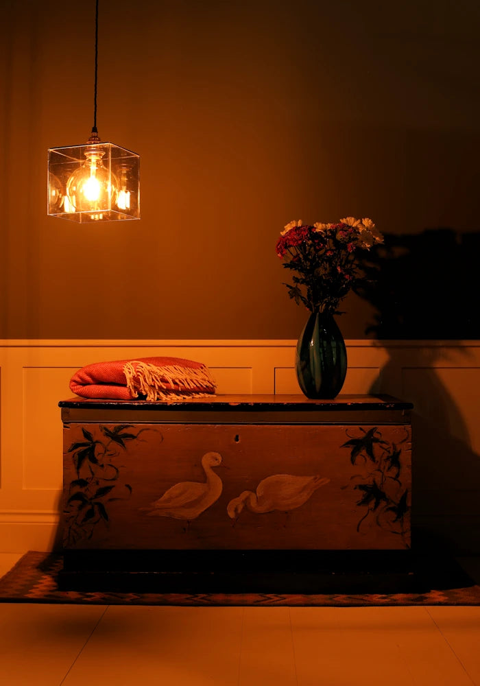 Glass pendant light, decorative chest with floral arrangement and lamp in a warm-toned room
