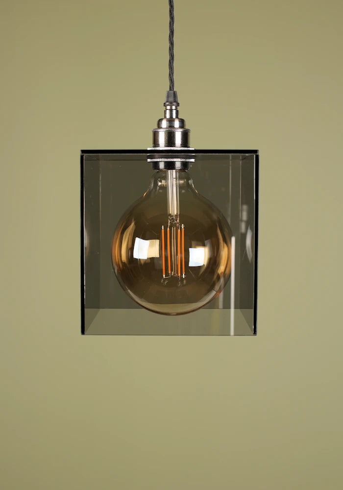 Vintage-style pendant light with a smoked glass shade, nickel lamp holder and exposed bulb against a green background