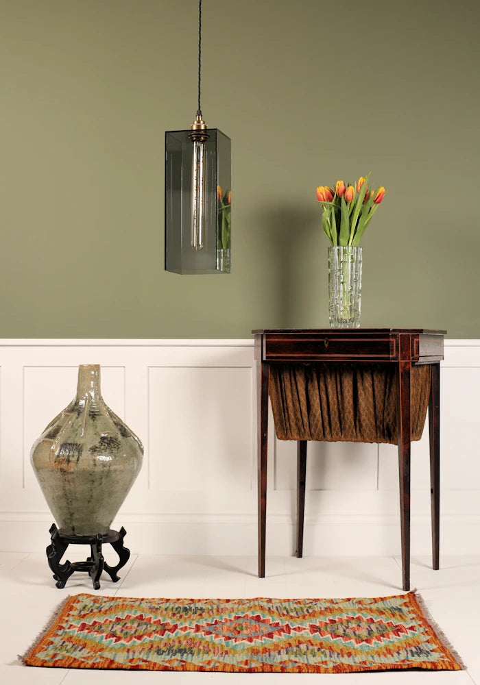 Large smoked glass pendant light, vintage dresser table with tulips, ornate floor vase on sage green background