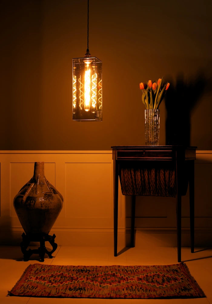 Large smoked glass pendant light, vintage dresser table with tulips, ornate floor vase in dimly lit room