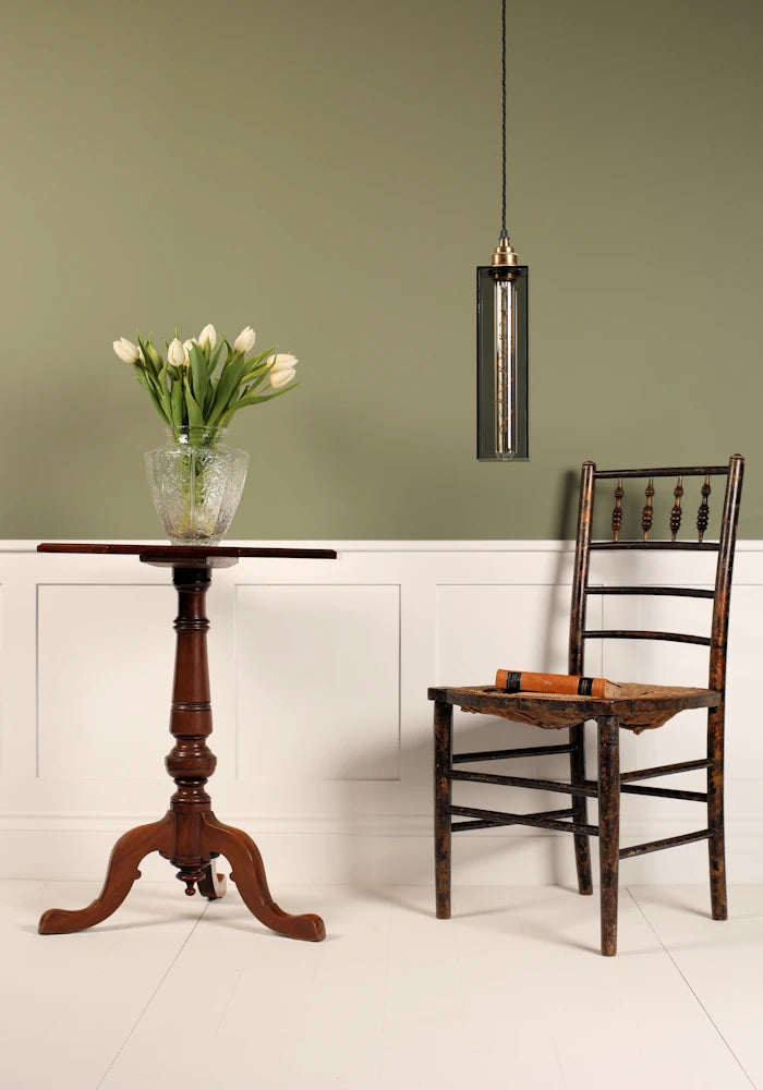 Elegant smoked glass pendant light hanging over chair, tall table with vase of tulips with sage green background