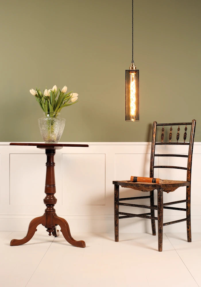 Elegant smoked glass pendant light hanging over chair, tall table with vase of tulips with sage green background