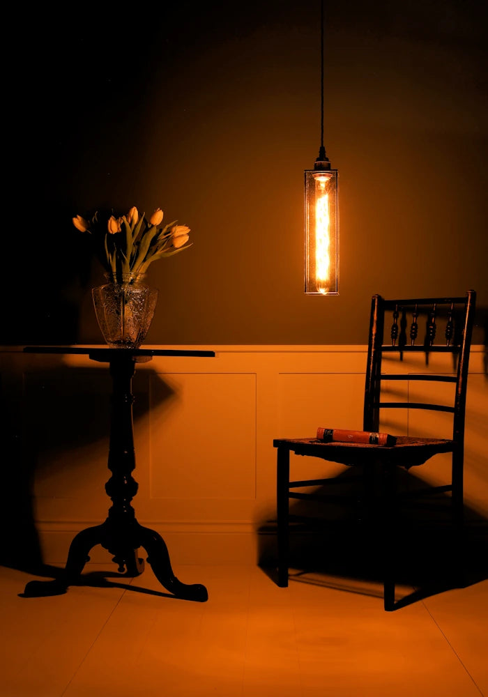 Elegant smoked glass pendant light hanging over chair, tall table with vase of tulips in dimly lit room