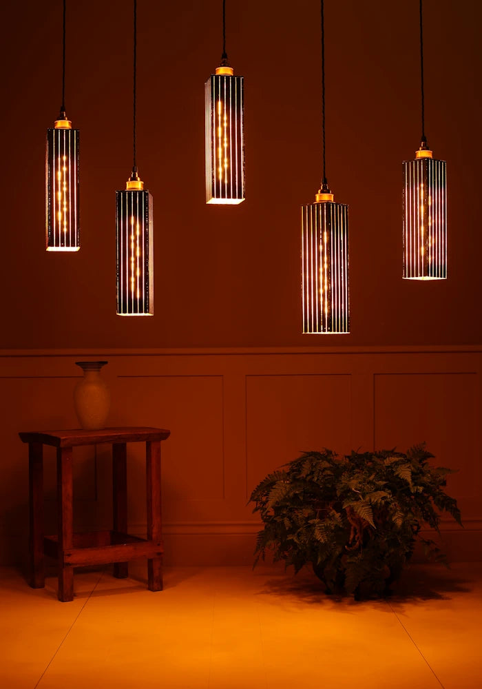 Modern pendant lights hanging against a warm-toned wall with a plant and wooden table in the foreground.