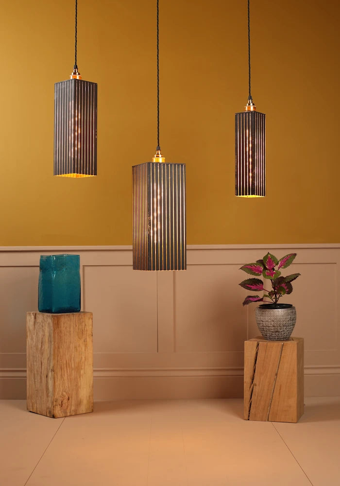 Three pendant lights hanging against a mustard yellow wall with wooden stands and decorative items.