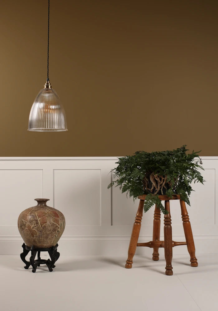 Bell shaped prismatic glass pendant light hanging over decorative vase, stool with green plant, beige background