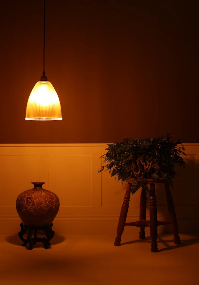 Bell shaped prismatic glass pendant light hanging over decorative vase, stool n dimly lit room