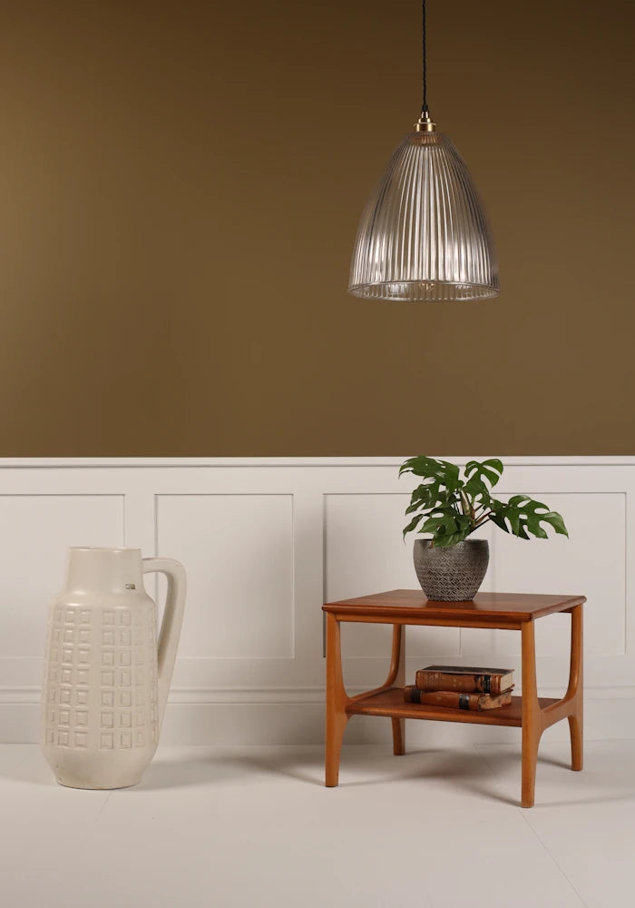 Large statement ribbed glass pendant light hanging over coffee table with plant, tall vase on beige background