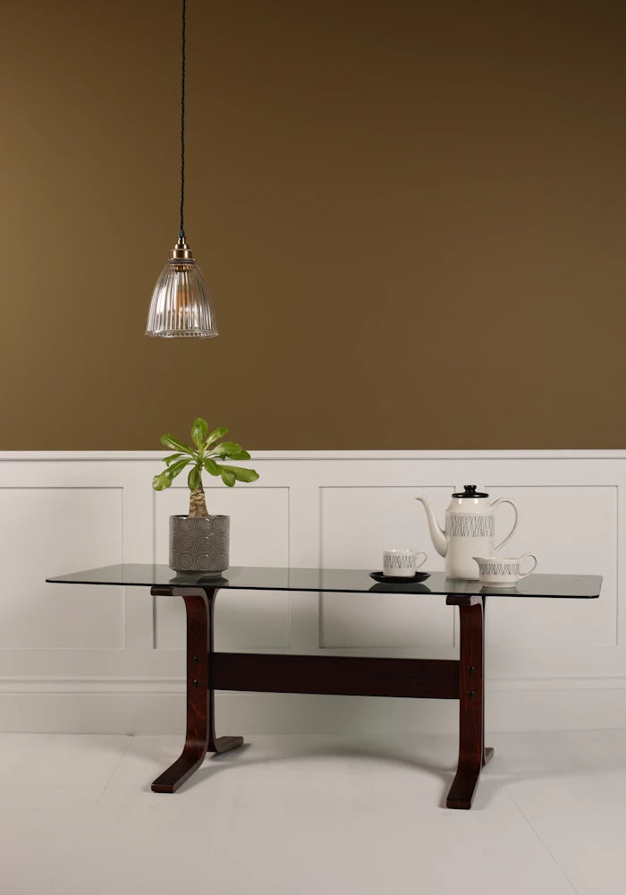 Small bell prismatic pendant light hanging over modern coffee table, plant, coffee pot on beige background