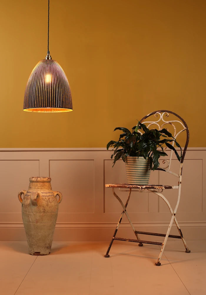 Pendant light fixture hanging above a small table with a plant against a mustard yellow wall.
