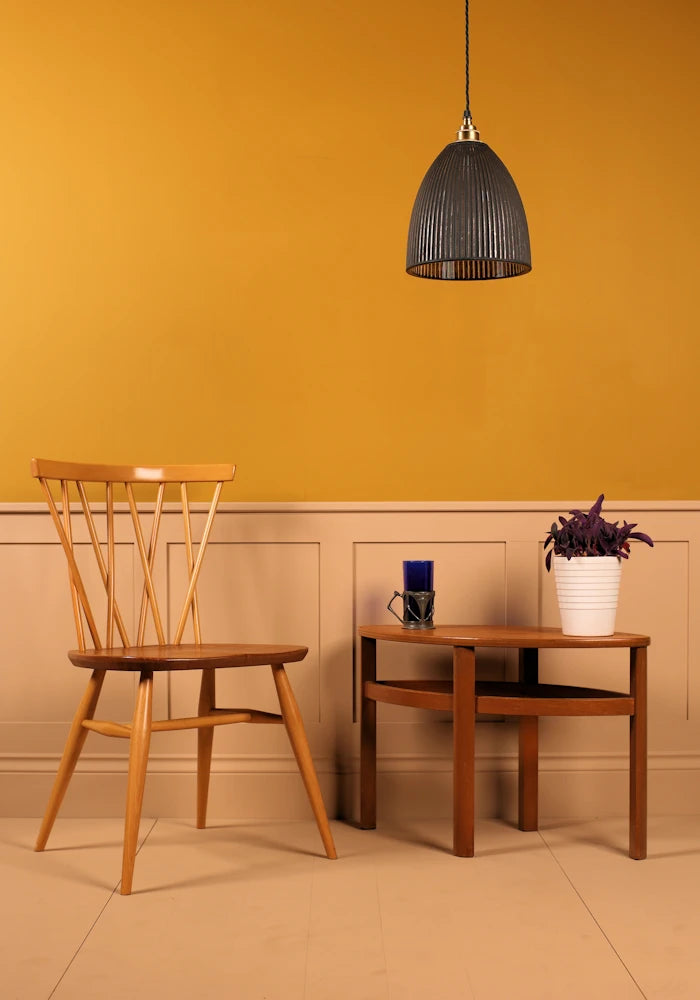 Black pendant light hanging over wooden table with plant, designer wooden chair and yellow background