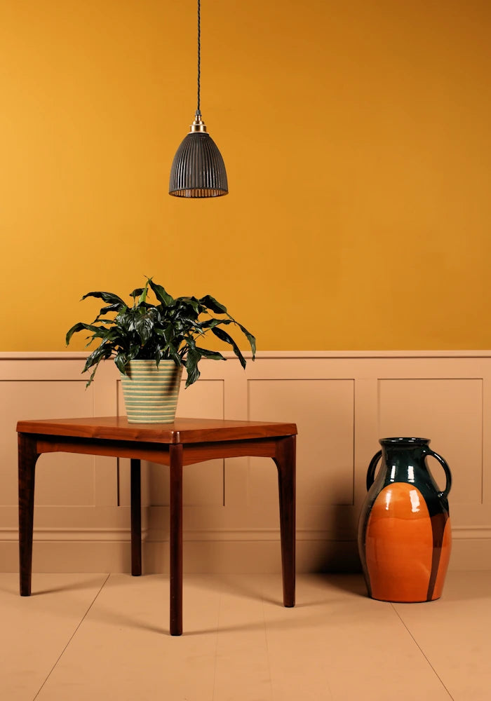Black fluted glass pendant light, wooden table with a plant and a decorative vase against an orange wall.