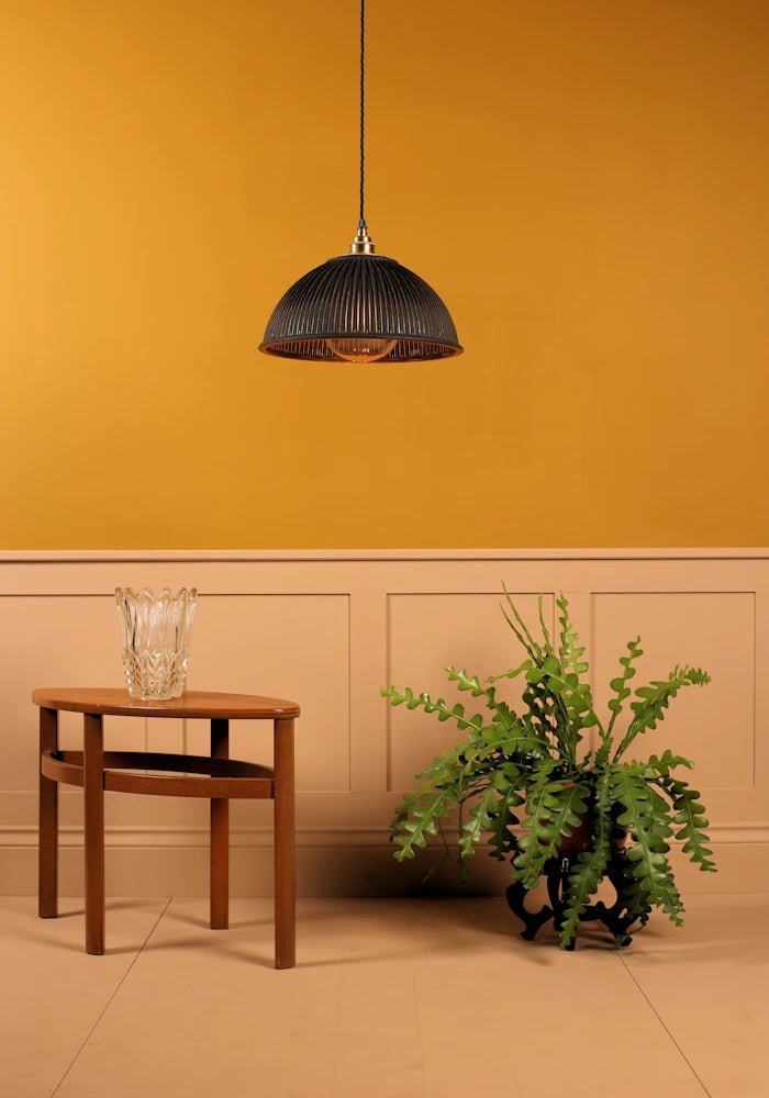 Black & gold dome prismatic glass pendant light hanging over coffee table, green leaf plant, on mustard yellow background