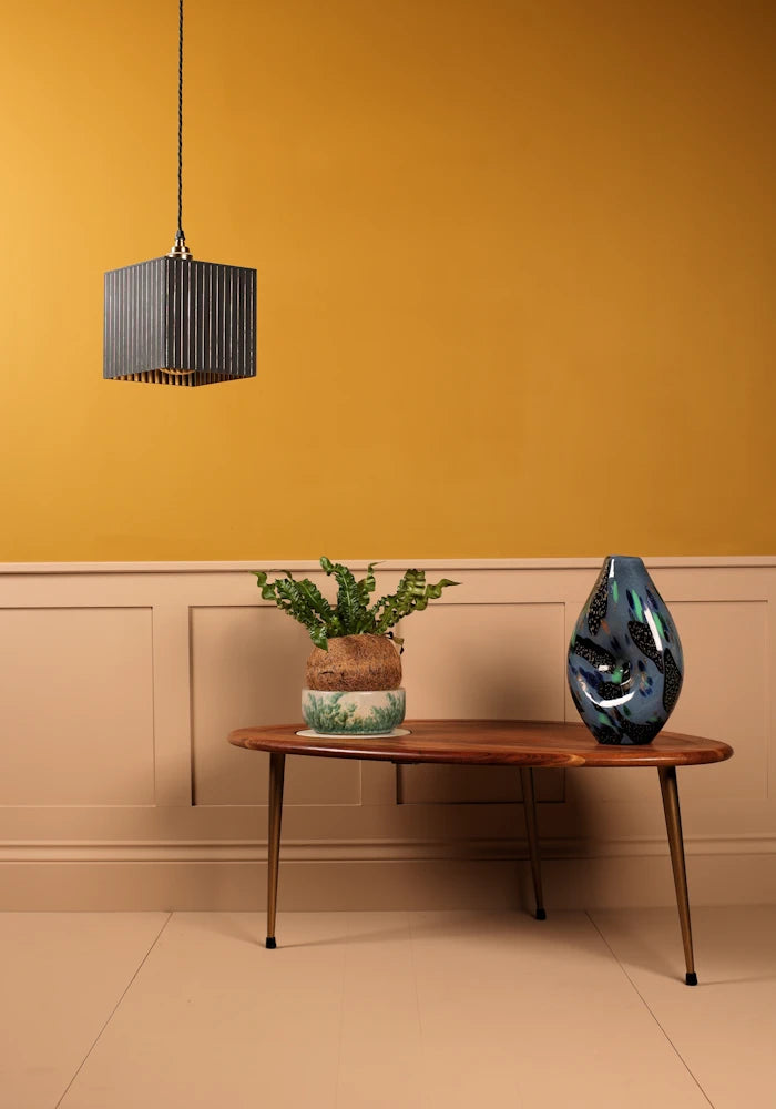 Modern interior with a wooden table, decorative vase, and pendant light against a mustard yellow wall.