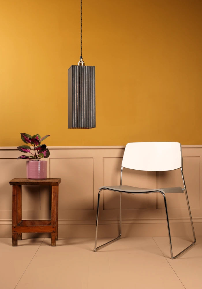 Large black pendant light with modern chair, plant and mustard coloured background