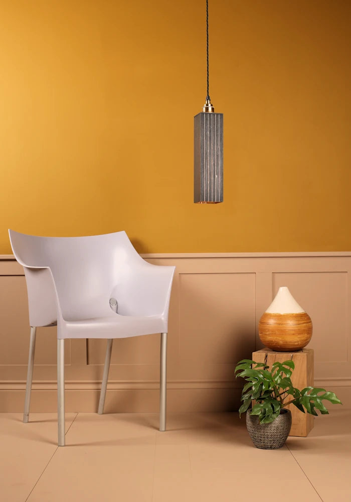 White chair against a mustard yellow wall with a pendant light and decorative items.