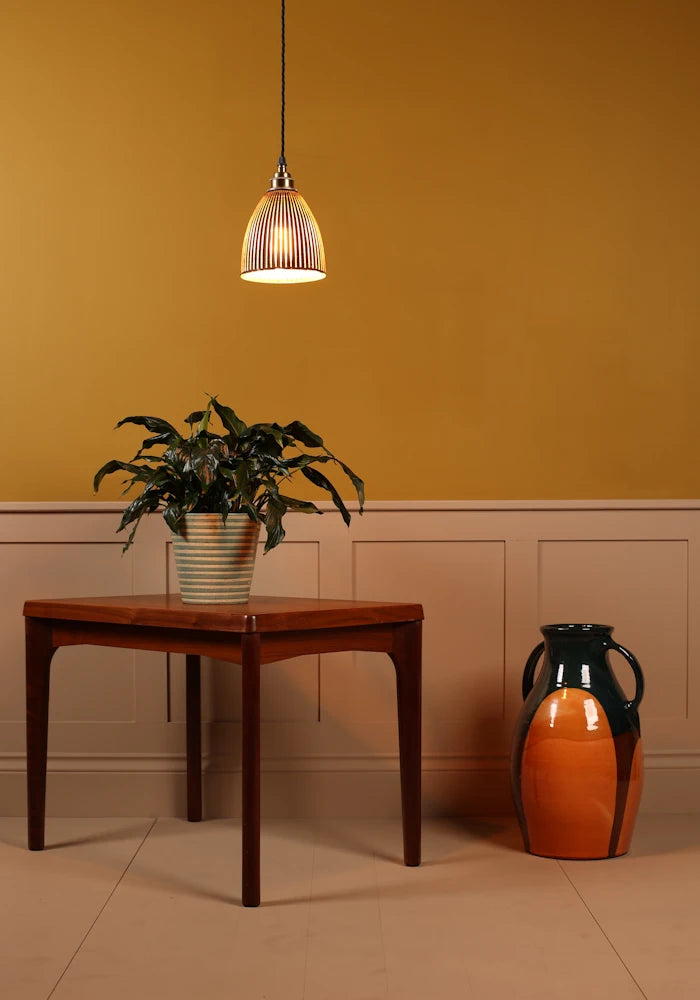 Black fluted glass pendant light, wooden table with a plant and a decorative vase against an orange wall.