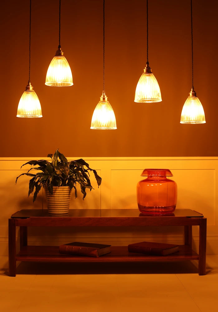 Cluster of prismatic glass pendant lights hanging over coffee table with vase, plant in dimly lit room