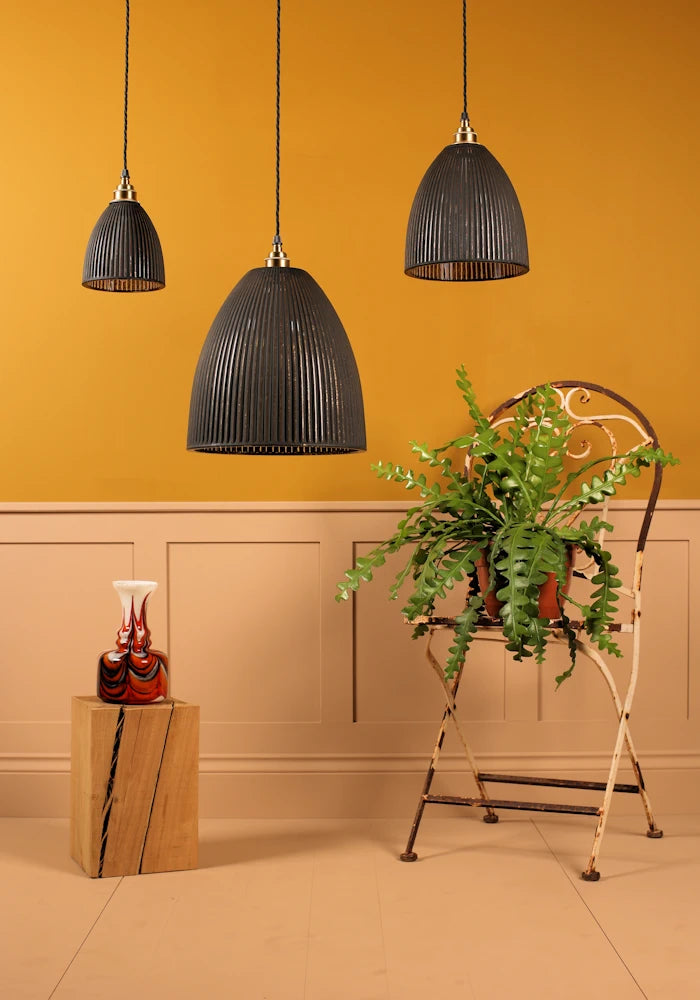 Three black pendant lights hanging against a mustard yellow wall with a plant and decorative items on a wooden stand.