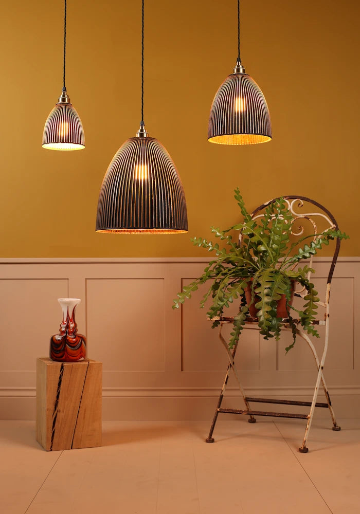 Three pendant lights hanging against a yellow wall with a plant and decorative items on a wooden block.