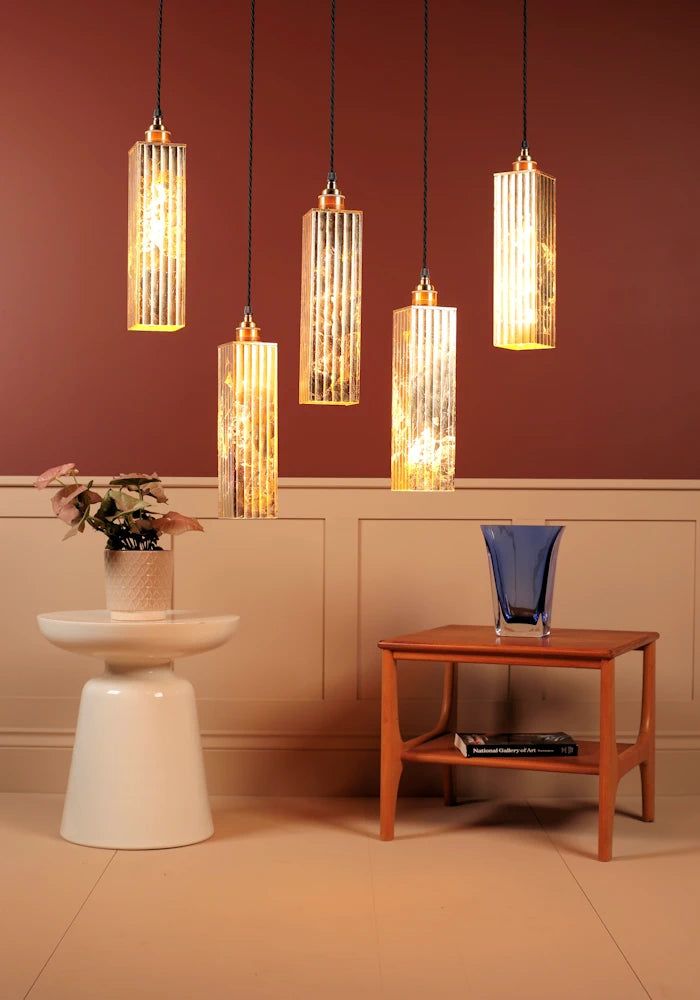 Five pendant lights hanging above a room with a white wall and wooden table.