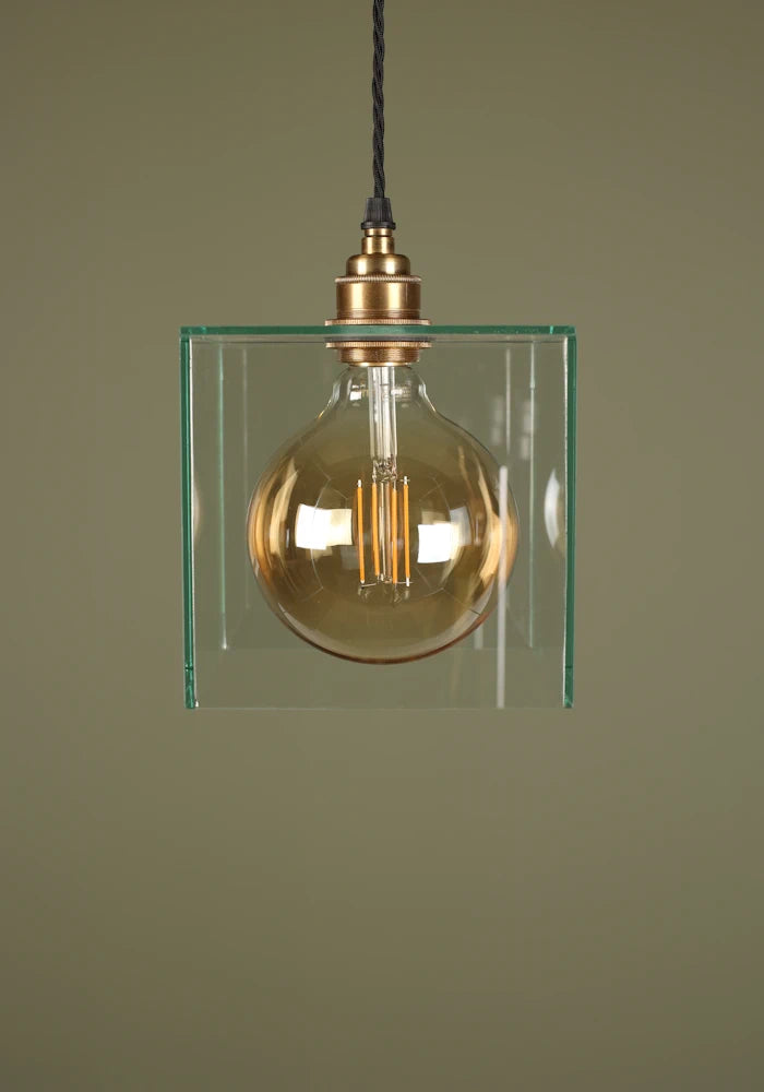 Clear glass cube pendant light with exposed light bulb, brass lamp holder on sage green background
