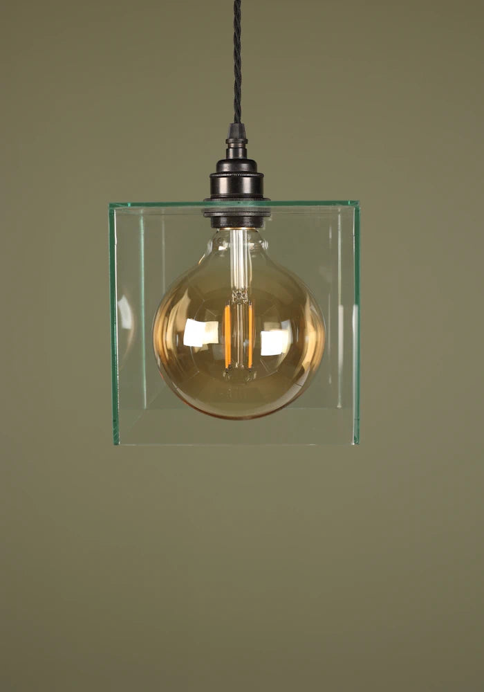 Clear glass cube pendant light with exposed light bulb, bronze lamp holder on sage green background