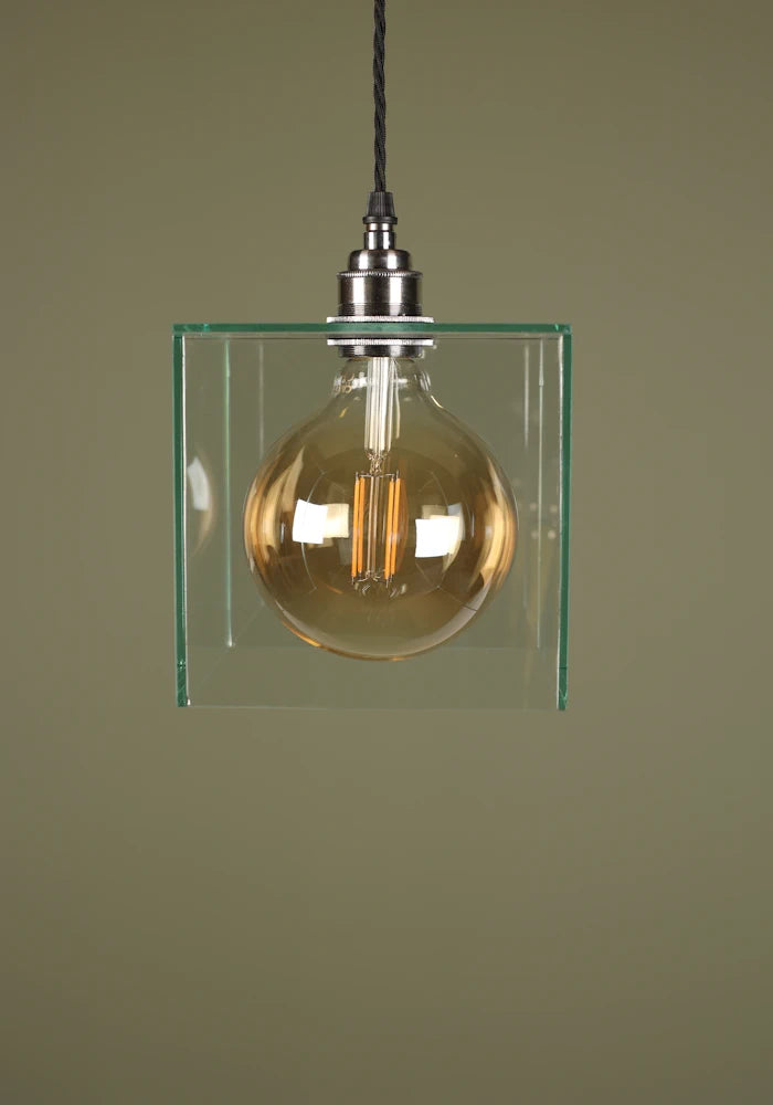 Clear glass cube pendant light with exposed light bulb, nickel lamp holder on sage green background