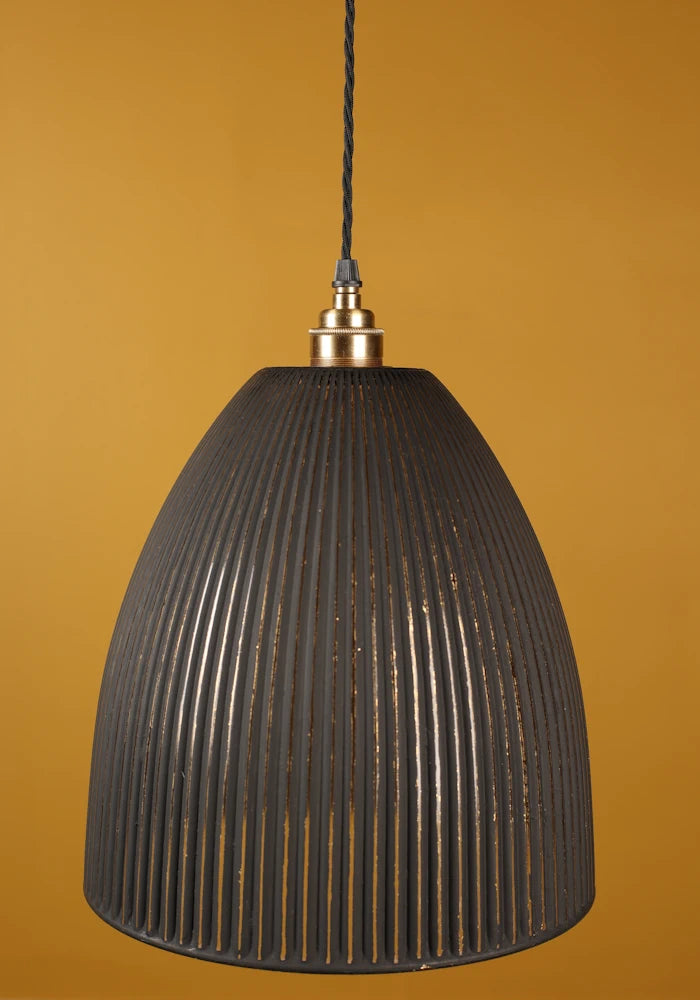 Black ribbed pendant light with brass lamp holder against a mustard yellow background